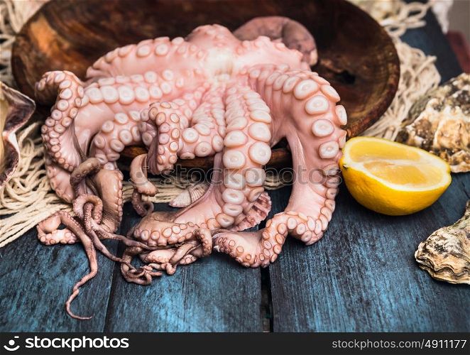 Raw octopus in wooden bowl with lemon on blue table