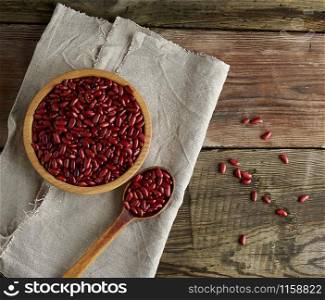 raw oval red beans in a plate on a wooden table. Organic meal. Vegetarian healthy natural food.
