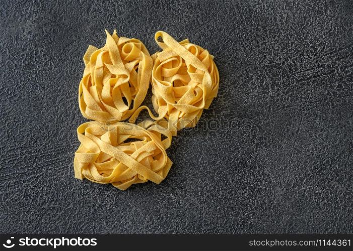 Raw pappardelle - flat Italian pasta noodles on wooden background