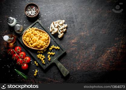 Raw pasta in bowl with mushrooms, tomatoes and spices. On dark rustic background. Raw pasta in bowl with mushrooms, tomatoes and spices.