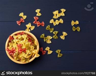 raw pasta in the form of bows in a wooden round plate and white textile napkin on a blue wooden background, top view. Vegetarian nutrition. Italian cuisine, copy space