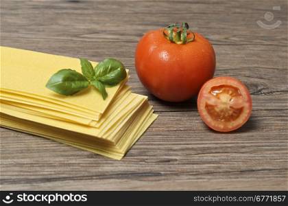 Raw pasta lasagna with basil leaves and fresh tomatoes on wooden background