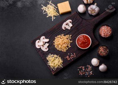 Raw pasta, mushrooms, onions, mince, spices and herbs to make a delicious paste with tomato sauce against a dark concrete background. Raw pasta, mushrooms, onions, mince, spices and herbs to make a delicious paste