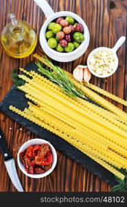 raw pasta, olives and dry tomato on a table