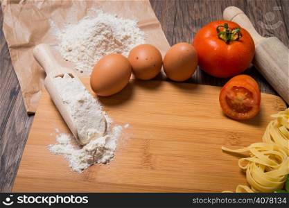 Raw pasta, tomato and eggs on wood background.