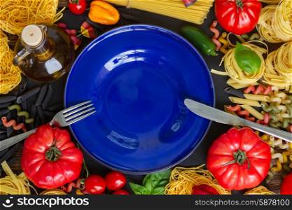Raw pasta with ingridients and blue plate. Raw pasta with ingridients and copy space on empty blue plate with fork and knife