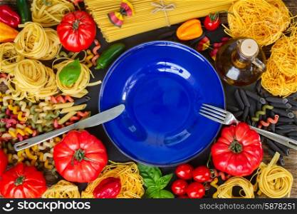 Raw pasta with ingridients and blue plate. Raw pasta with ingridients and copy space on empty blue plate with steel fork and knife