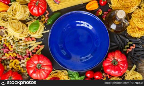 Raw pasta with ingridients and copy space on empty blue plate. Raw pasta with ingridients and blue plate