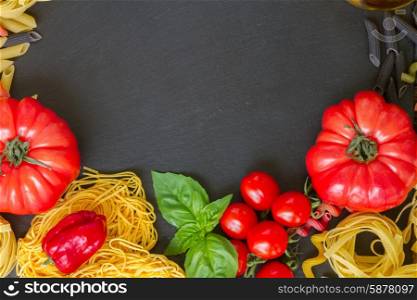 Raw pasta with ingridients on black board. Pasta with tomatoes and copy space on black board
