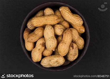 Raw peanuts shells in bowl over dark background