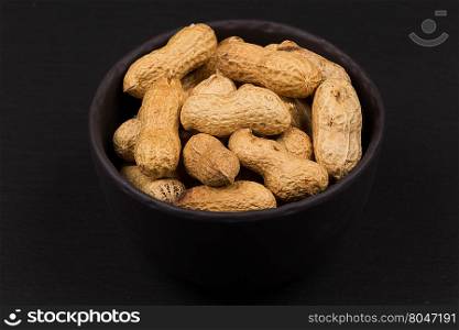 Raw peanuts shells in bowl over dark background