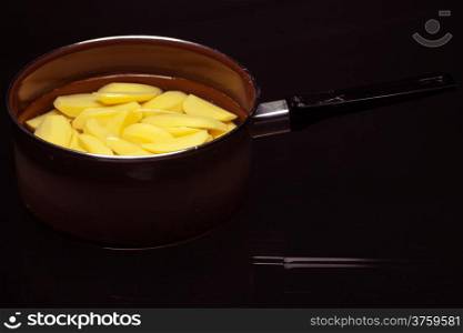 Raw peeled potatoes in pot or pan on black. Healthy food and cooking.