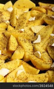 Raw peeled potatoes with spices, butter slices ready to be roasted as background