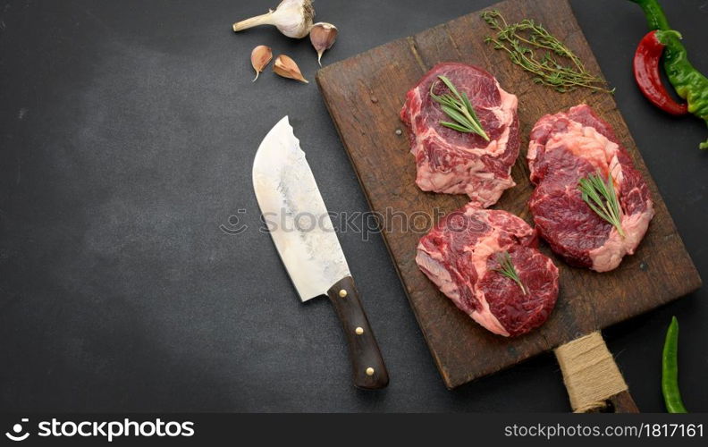 raw piece of beef ribeye with rosemary, thyme on a black table, top view, copy space