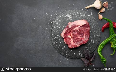 raw piece of beef ribeye with rosemary, thyme on a black table, top view, copy space