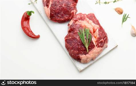 raw piece of beef ribeye with rosemary, thyme on a white table, top view