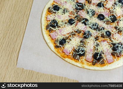 Raw pizza with olives, ham, bacon, mushrooms and grated cheese