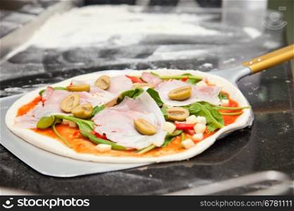raw pizza with spinach, olives, ham