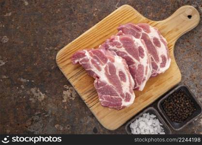 raw pork chop fillet in wooden cutting board with salt and pepper on rusty texture background with copy space for text, top view, flat lay