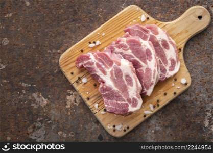 raw pork chop fillet with salt and pepper in wooden cutting board on rusty texture background with copy space for text, top view