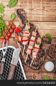 Raw pork kebab with paprika on chopping board with fresh vegetables and disposable charcoal grill on wooden background with fork and knife. Salt and pepper with lettuce and paprika.