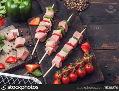 Raw pork kebab with paprika on chopping board with fresh vegetables and disposable charcoal grill on wooden background. Salt and pepper with lettuce and paprika pepper.