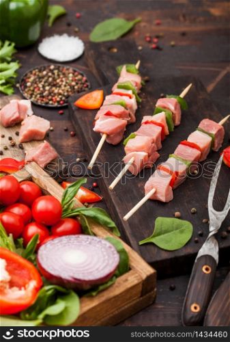 Raw pork kebab with paprika on chopping board with fresh vegetables on wooden background with fork. Salt and pepper with lettuce and paprika and cherry tomatoes.