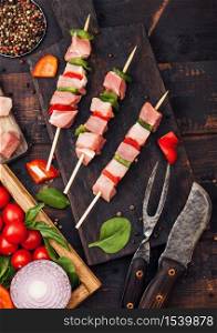 Raw pork kebab with paprika on chopping board with fresh vegetables on wooden background with fork and knife. Salt and pepper with lettuce and paprika and cherry tomatoes.