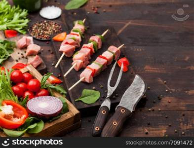 Raw pork kebab with paprika on chopping board with fresh vegetables on wooden background with fork and knife. Salt and pepper with lettuce and paprika and cherry tomatoes.