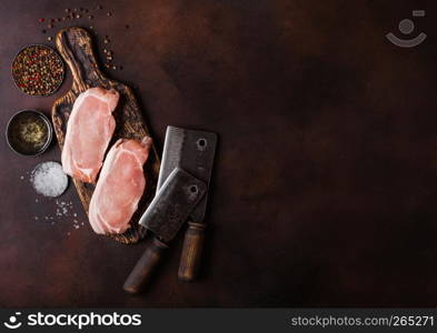 Raw pork loin chops on old vintage chopping board with knife and fork on rusty background. Salt and pepper with fresh rosemary and oil.