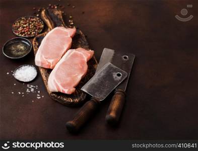 Raw pork loin chops on old vintage chopping board with knife and fork on rusty background. Salt and pepper with fresh rosemary and oil.