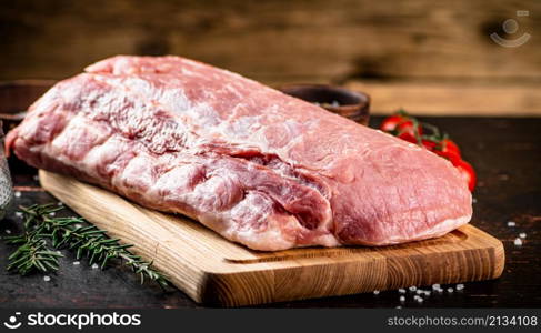 Raw pork on a cutting board with fresh tomatoes. On a wooden background. High quality photo. Raw pork on a cutting board with fresh tomatoes.