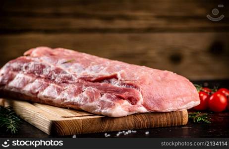 Raw pork on a cutting board with fresh tomatoes. On a wooden background. High quality photo. Raw pork on a cutting board with fresh tomatoes.