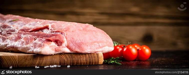 Raw pork on a cutting board with fresh tomatoes. On a wooden background. High quality photo. Raw pork on a cutting board with fresh tomatoes.