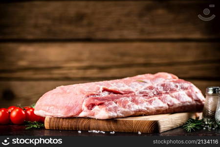 Raw pork on a cutting board with fresh tomatoes. On a wooden background. High quality photo. Raw pork on a cutting board with fresh tomatoes.