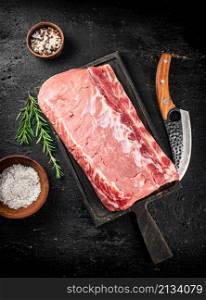 Raw pork on a cutting board with spices and a knife. On a black background. High quality photo. Raw pork on a cutting board with spices and a knife.