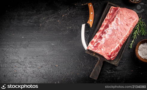 Raw pork on a cutting board with spices and a knife. On a black background. High quality photo. Raw pork on a cutting board with spices and a knife.