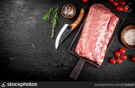 Raw pork on a cutting board with spices and a knife. On a black background. High quality photo. Raw pork on a cutting board with spices and a knife.