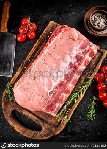 Raw pork on a cutting board with tomatoes, rosemary and spices. On a black background. High quality photo. Raw pork on a cutting board with tomatoes, rosemary and spices.