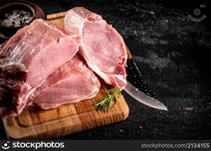 Raw pork on a spice cutting board. On a black background. High quality photo. Raw pork on a spice cutting board.