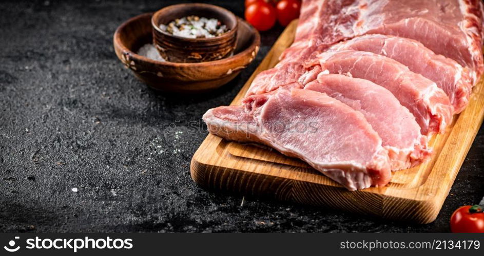 Raw pork on a spice cutting board. On a black background. High quality photo. Raw pork on a spice cutting board.