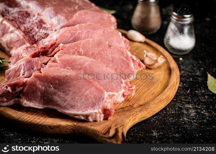 Raw pork on a spice cutting board. On a black background. High quality photo. Raw pork on a spice cutting board.