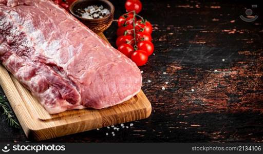 Raw pork on a wooden cutting board with tomatoes and spices. Against a dark background. High quality photo. Raw pork on a wooden cutting board with tomatoes and spices.