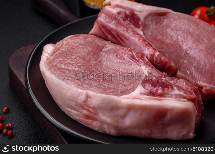 Raw pork on the bone or rib sliced with salt, spices and herbs on a dark concrete background