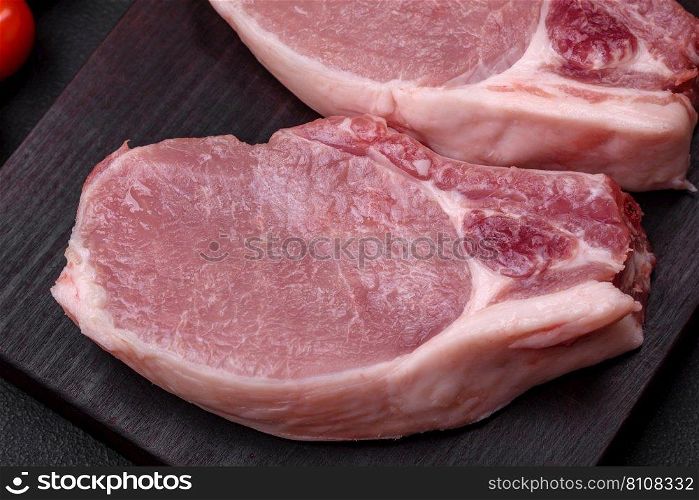 Raw pork on the bone or rib sliced with salt, spices and herbs on a dark concrete background