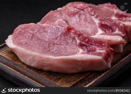 Raw pork on the bone or rib sliced with salt, spices and herbs on a dark concrete background