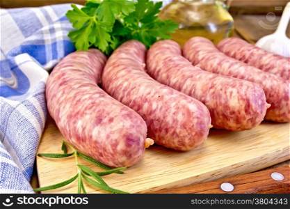 Raw pork sausage, knife, rosemary, parsley, oil, garlic and a napkin on the background of wooden boards