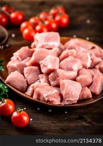 Raw pork sliced on a plate with tomatoes. On a wooden background. High quality photo. Raw pork sliced on a plate with tomatoes.