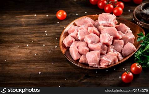 Raw pork sliced on a plate with tomatoes. On a wooden background. High quality photo. Raw pork sliced on a plate with tomatoes.