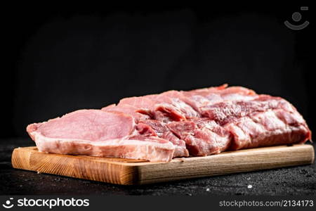 Raw pork sliced on a wooden cutting board. On a black background. High quality photo. Raw pork sliced on a wooden cutting board.